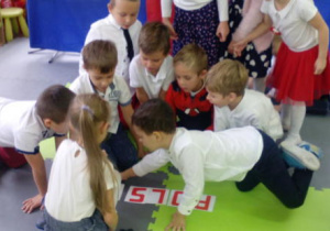 Grupka dzieci układa napis "Polska" z liter na dywanie.
